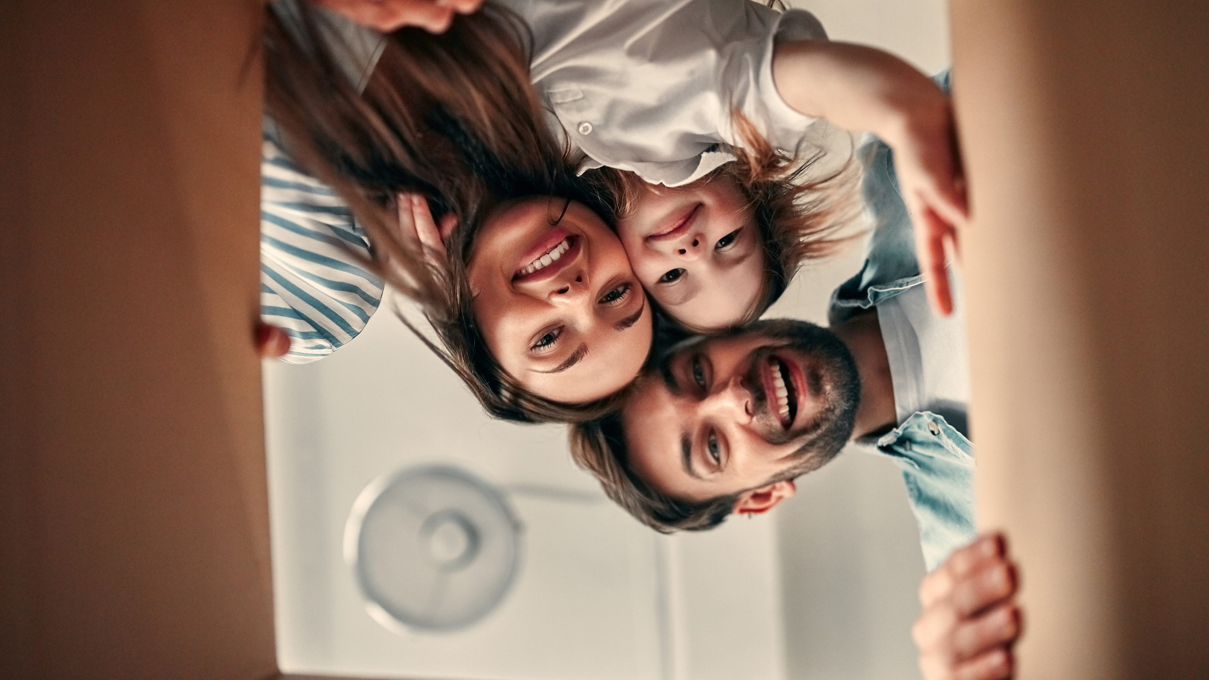 Family on moving day. Attractive young woman and handsome bearded man with their cute little daughter are happy to move into new home. Looking into cardboard box together.