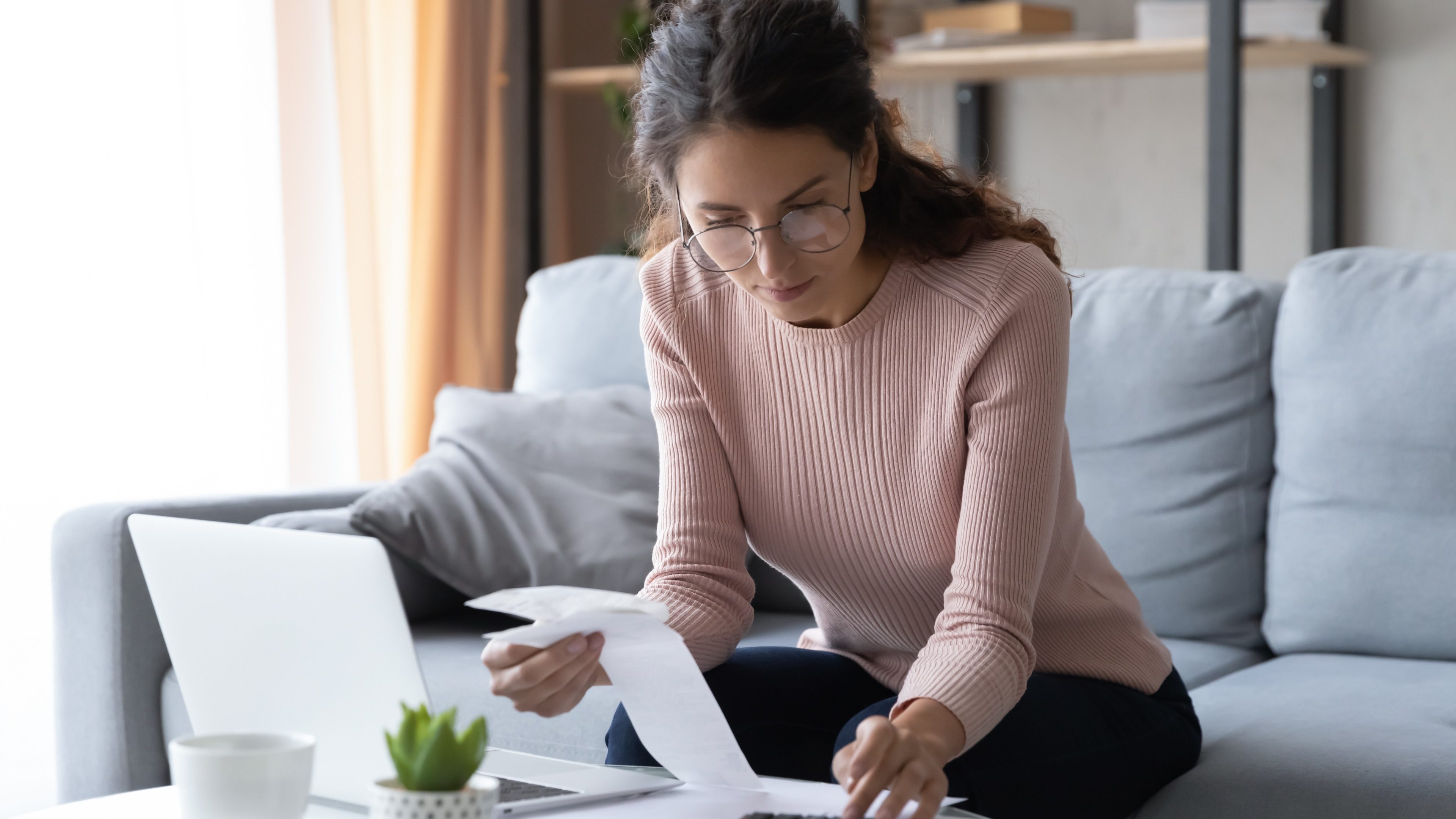 Focused smart millennial woman in eyeglasses busy with financial paperwork, calculating utility bills or taxes, managing monthly household budget or planning expenditures, bookkeeping concept.