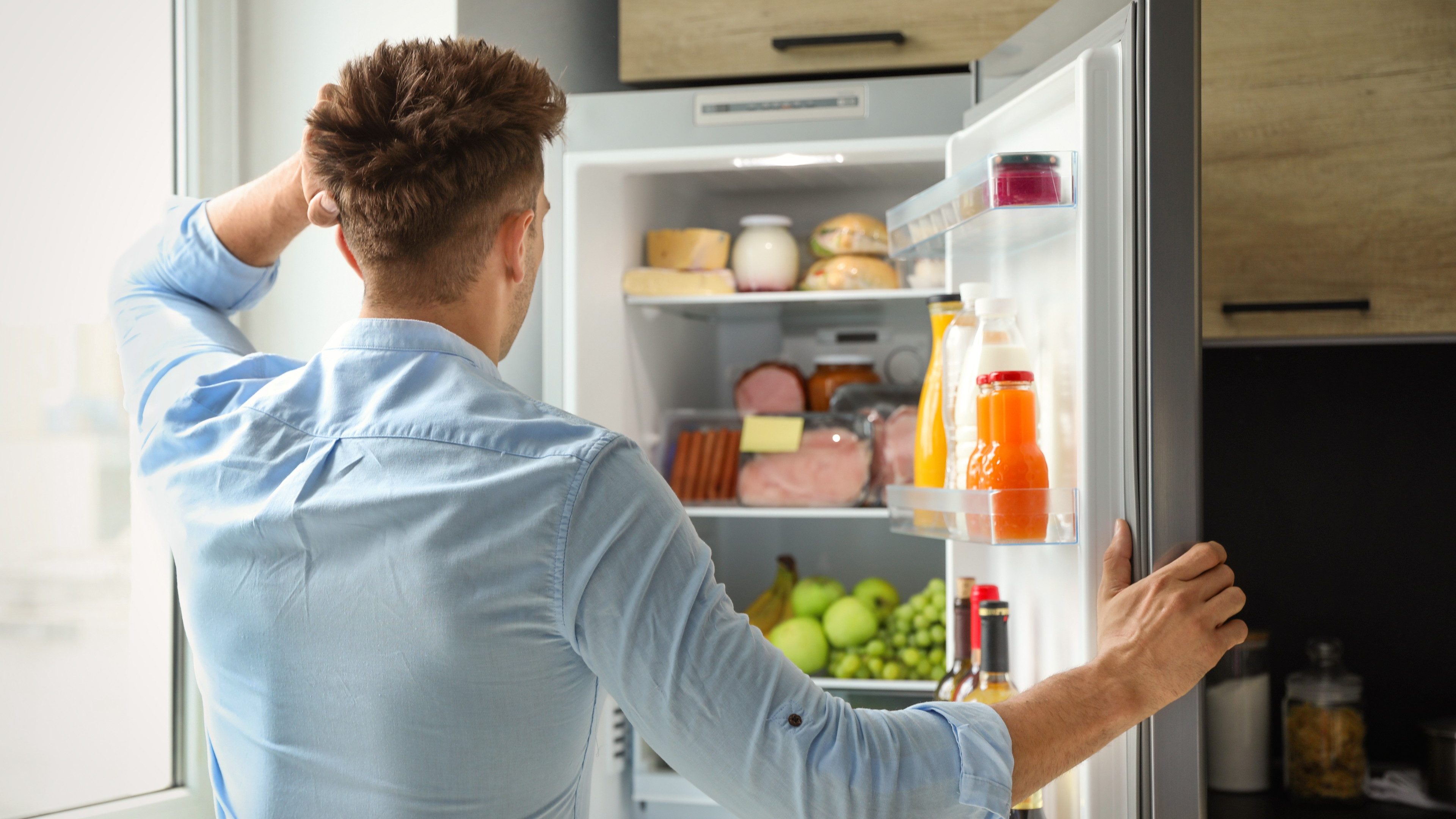 Man looking into refrigerator full of products in kitchen