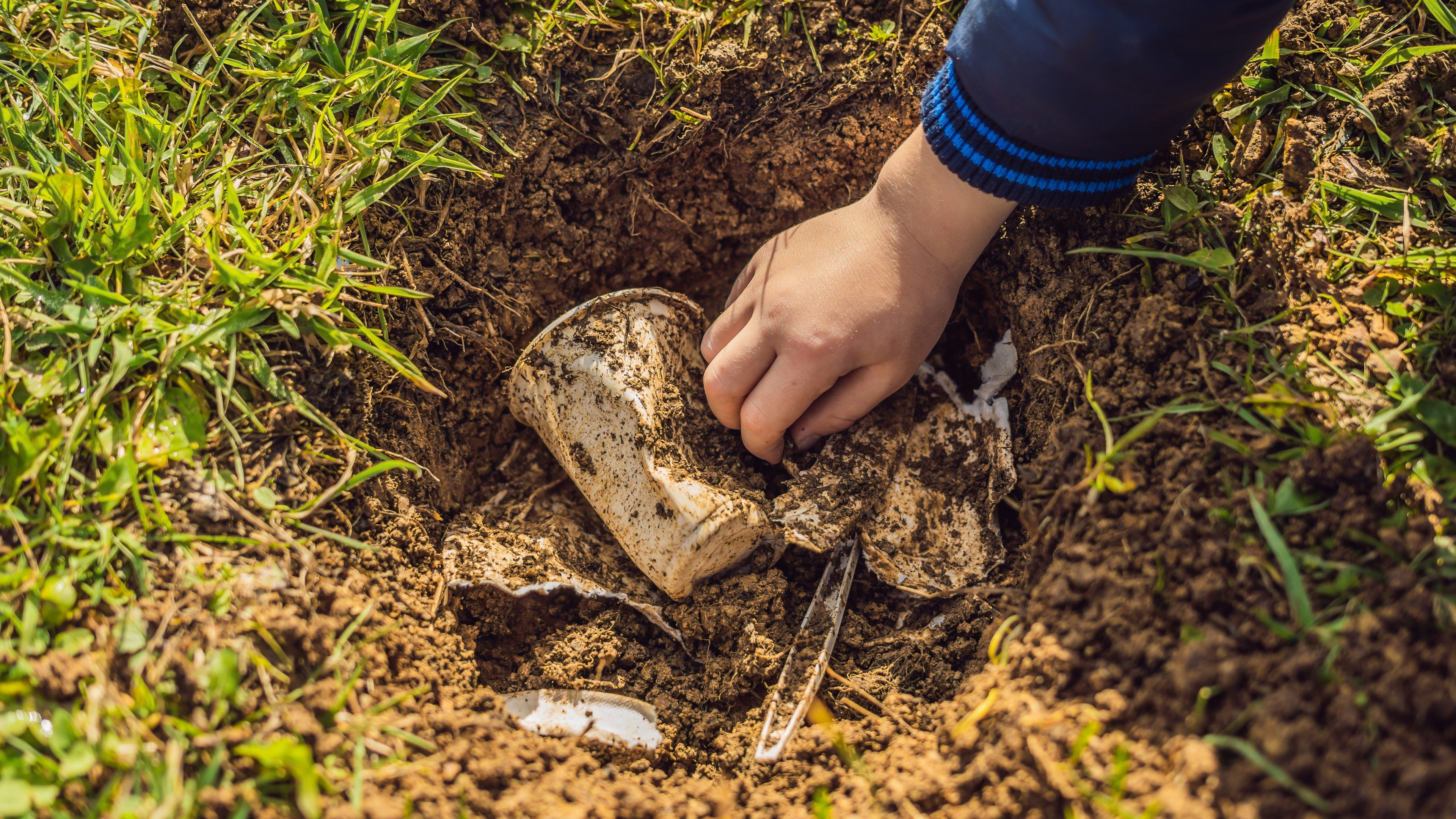 The boy plays recycling. He buries plastic disposable dishes and biodegradable dishes. After a few months, he dug up the dishes and saw that the biodegradable dishes began to decompose and plastic did