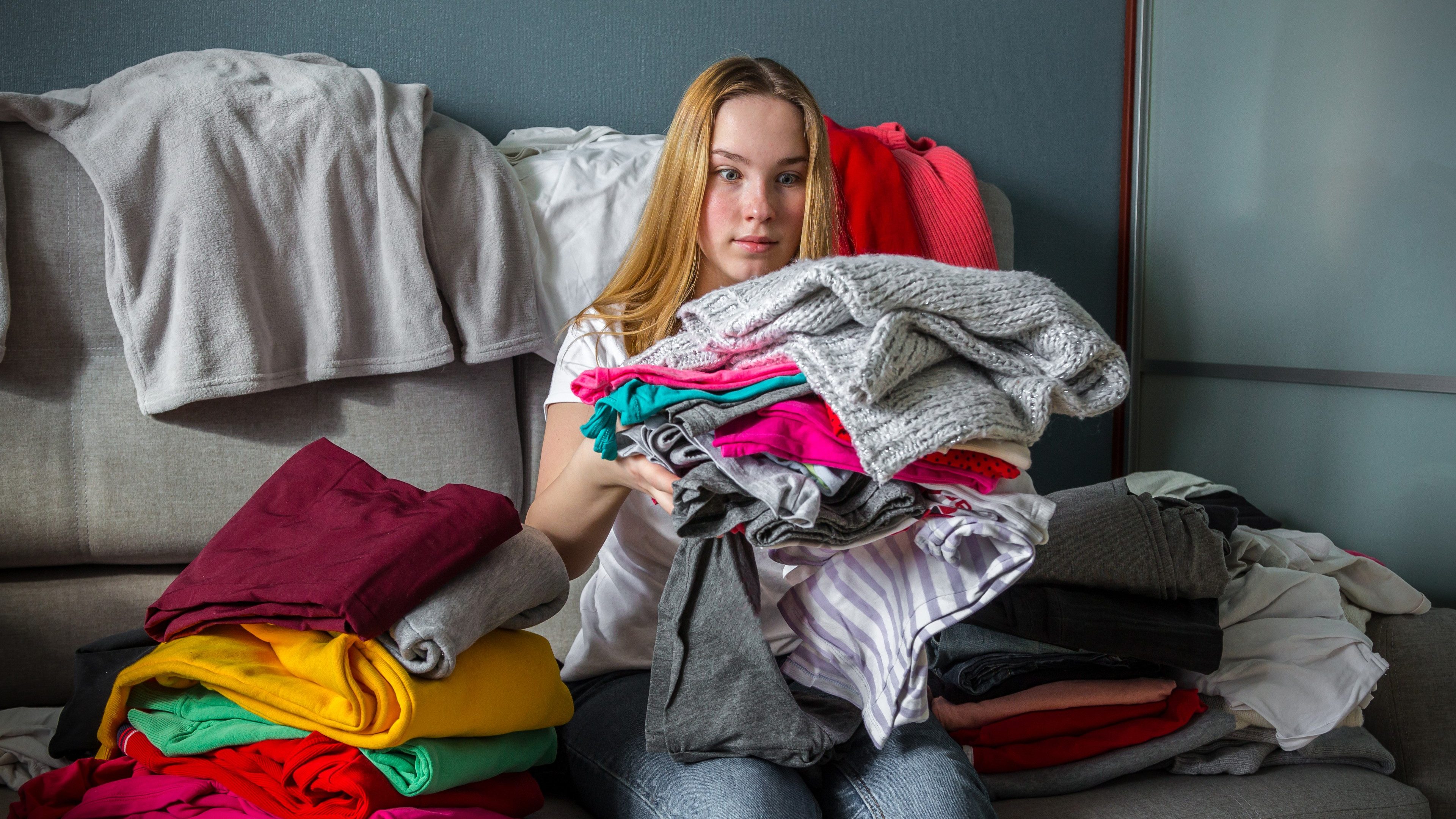 Fast fashion, the girl puts things in order in the closet. A bunch of colorful clothes. The concept of processing, second hand, eco, minimalism, consumption of goods.