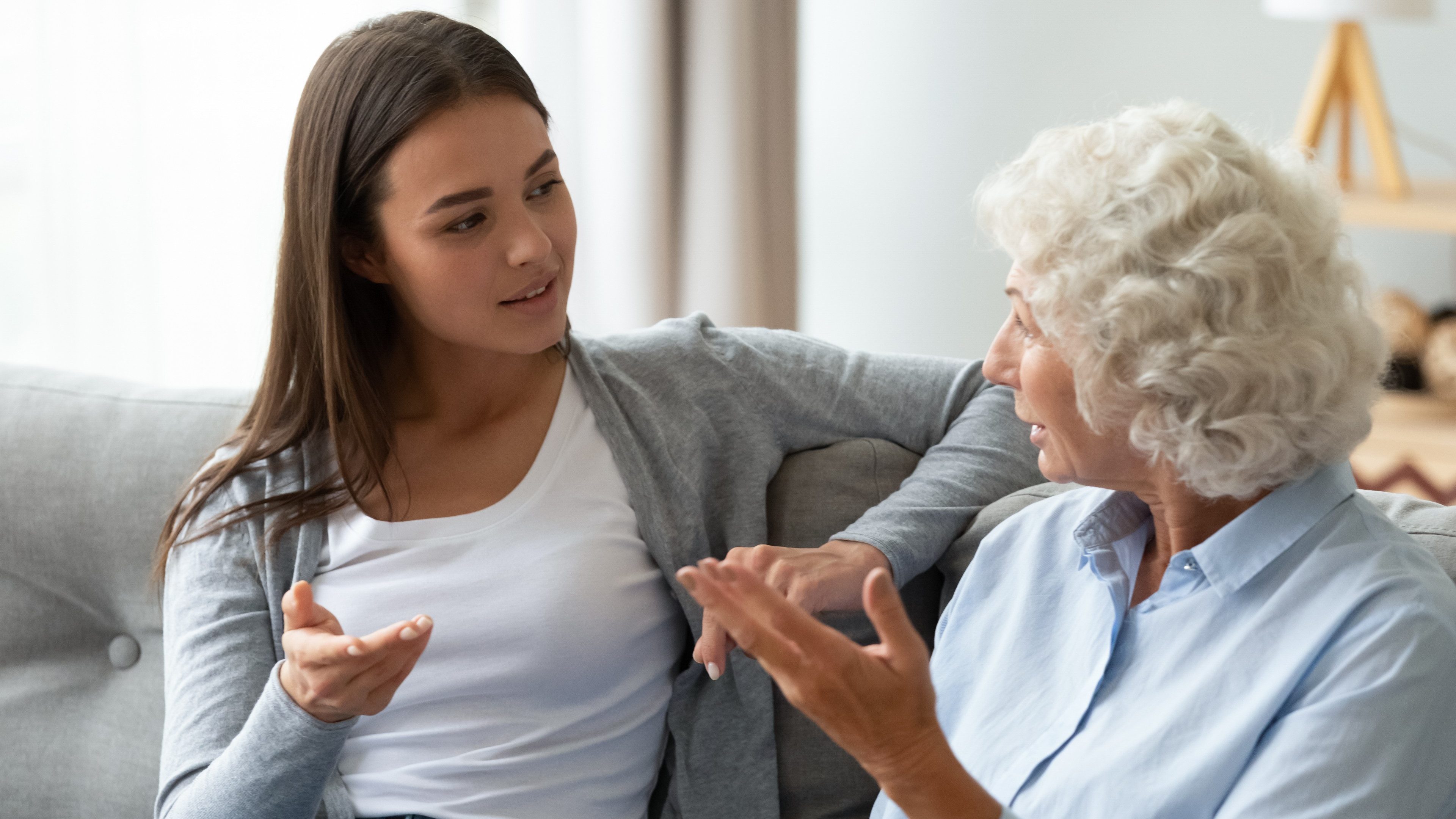 Mature woman sit on couch in living room talk chat with grown-up adult daughter at home, millennial girl have pleasant conversation with elderly middle-aged mother, share secret, gossip indoors