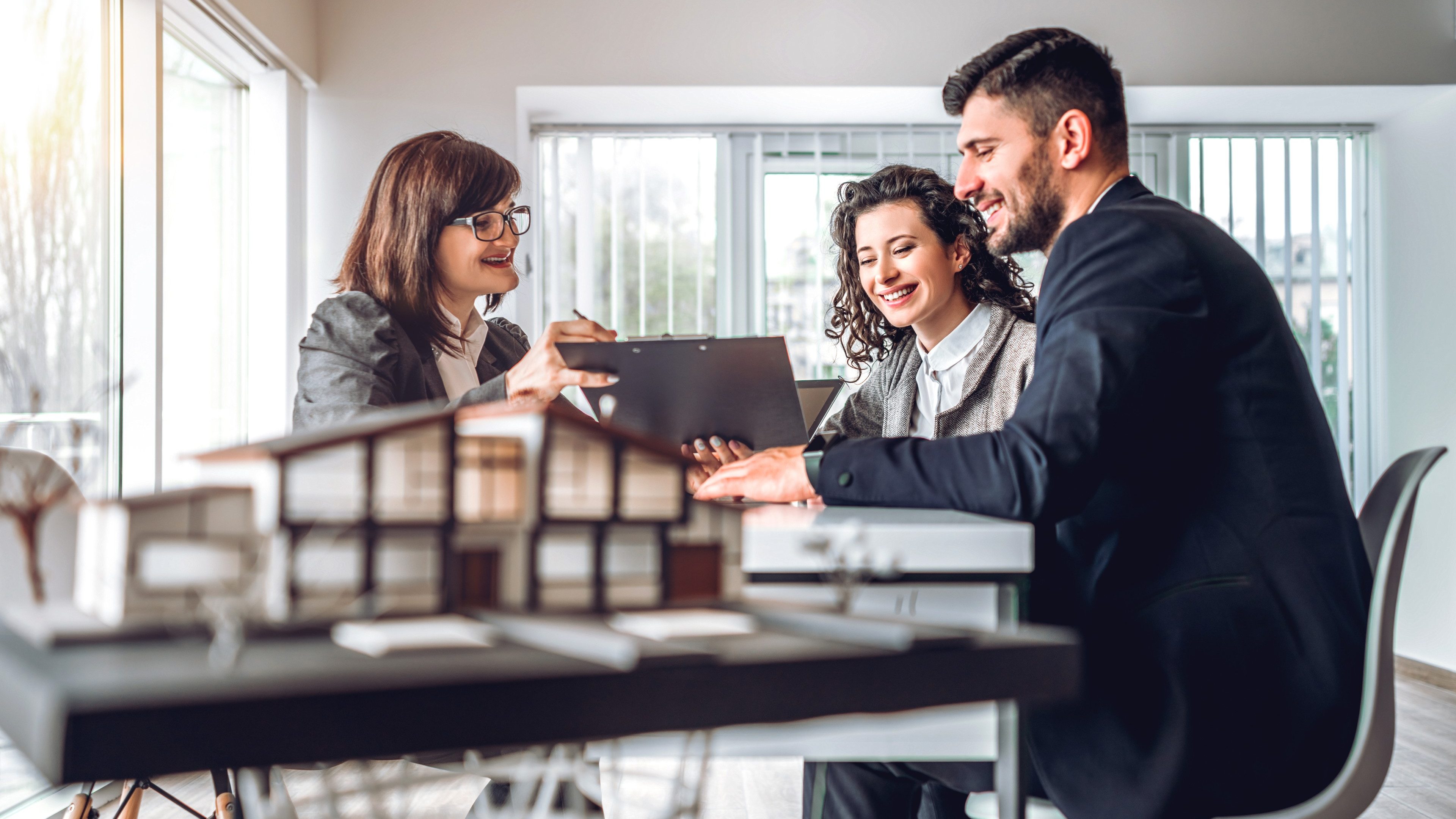 Side view image of young happy family sitting in consulting office, making property purchase. Mature realtor helping business couple do financial investment. Installment payment, mortgage loan concept