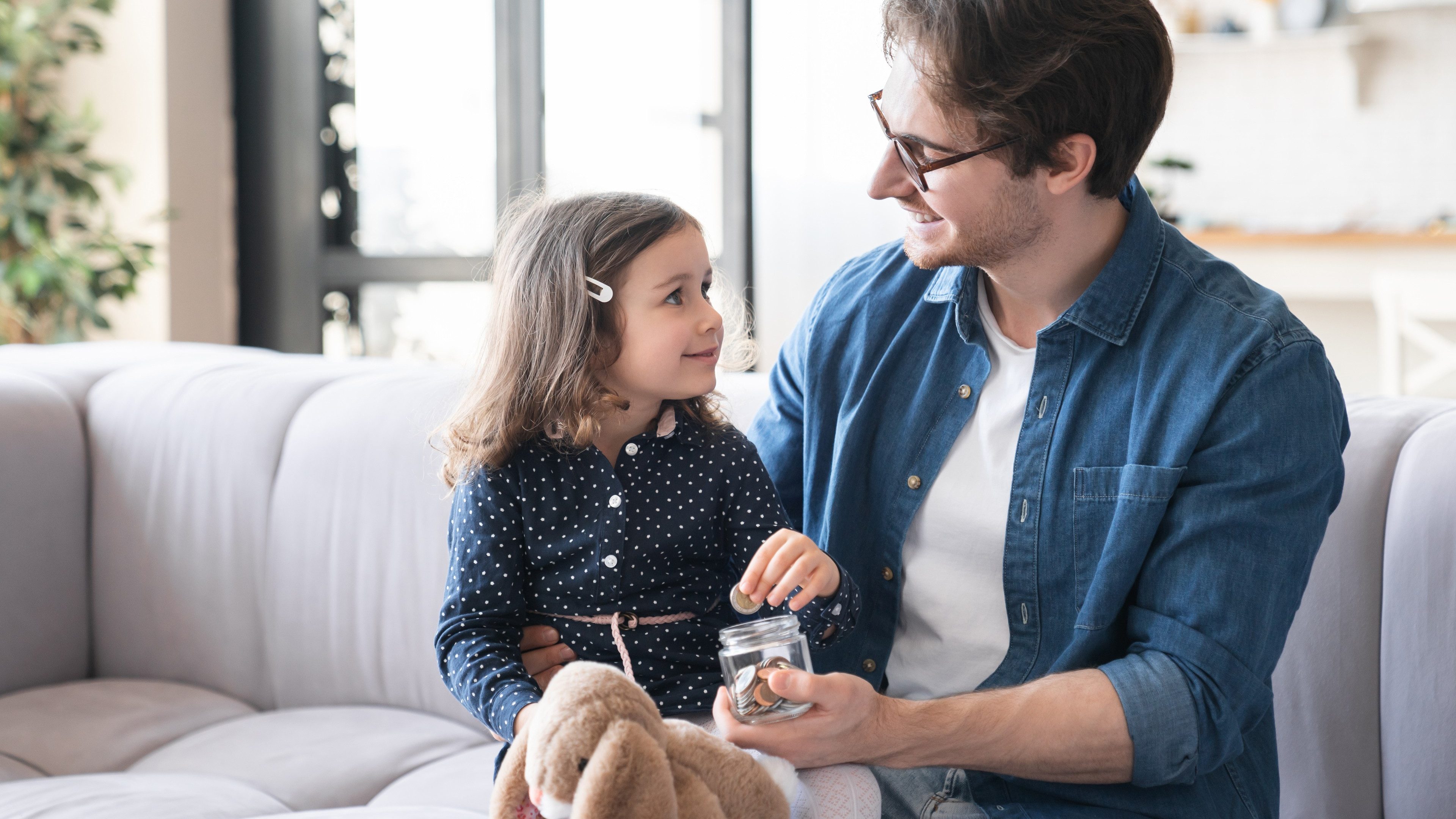 Small girl daughter and her young father putting money to the moneybox piggy bank. Personal Savings. Saving money concept. For future, mortgage loan savings home in crisis coronavirus concept.