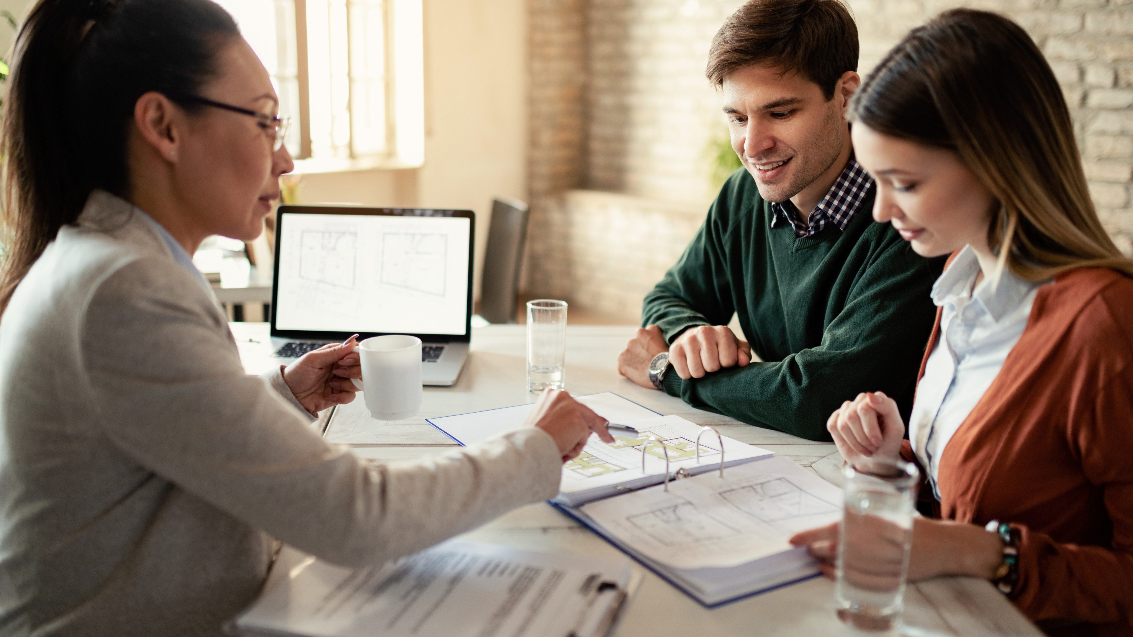 Smiling couple and insurance agent going through real estate plans during a meeting in the office. Focus is on man. 