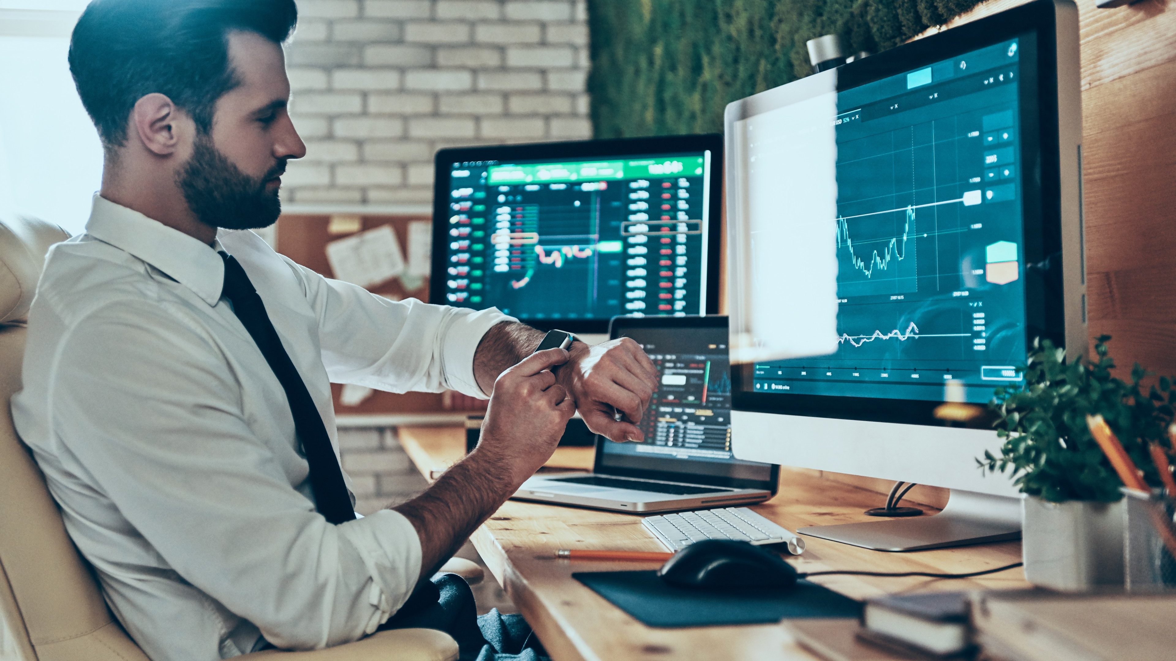 Busy young modern man in formalwear checking the time while sitting in the office