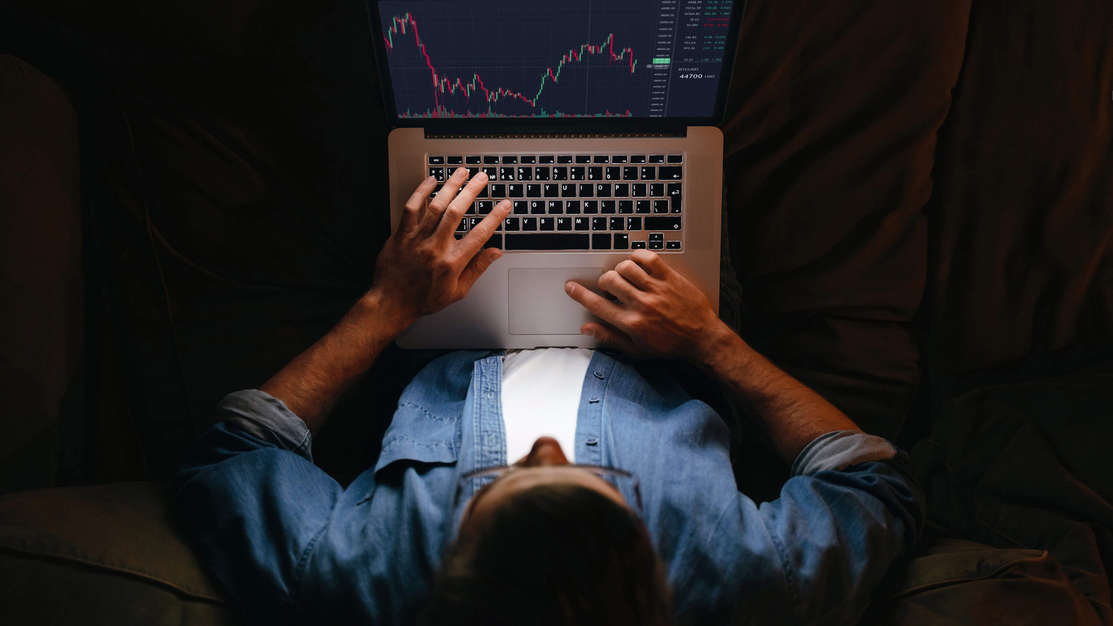 Mladý obchodník, analytik a investor sledujúci monitor notebooku na pohovke, maklér analyzujúci indexy, finančný graf, obchodovanie online, investičné údaje o kryptomenách a akciovom trhu.