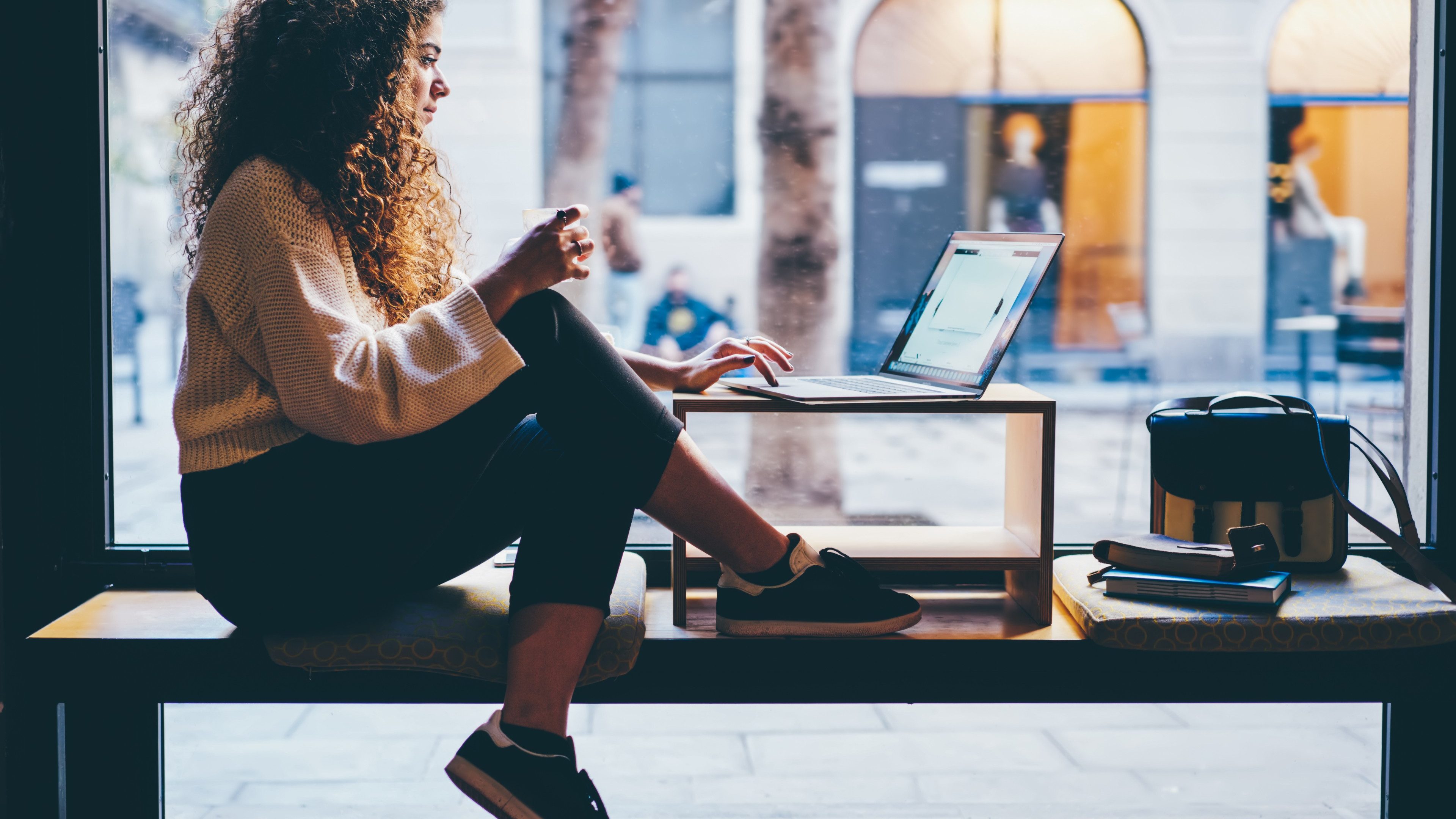 Young pondering female person with beautiful curly hair checking account balance on webpage.Talented student preparing for upcoming examinations during sitting next to copy space for your advertising