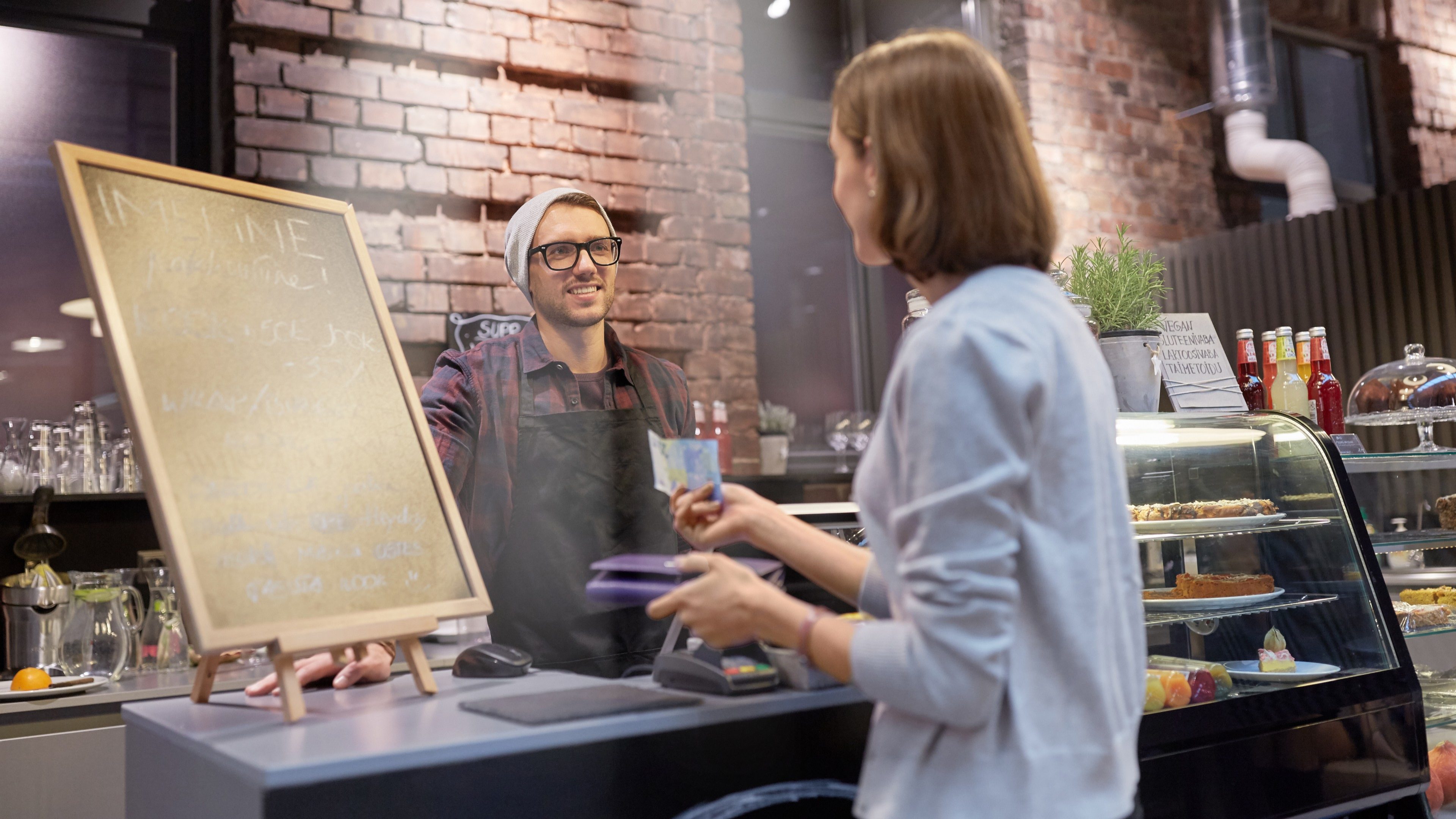 Mladá žena podáva hipsterskému predavačovi v kaviarni 20,- € bankovku.