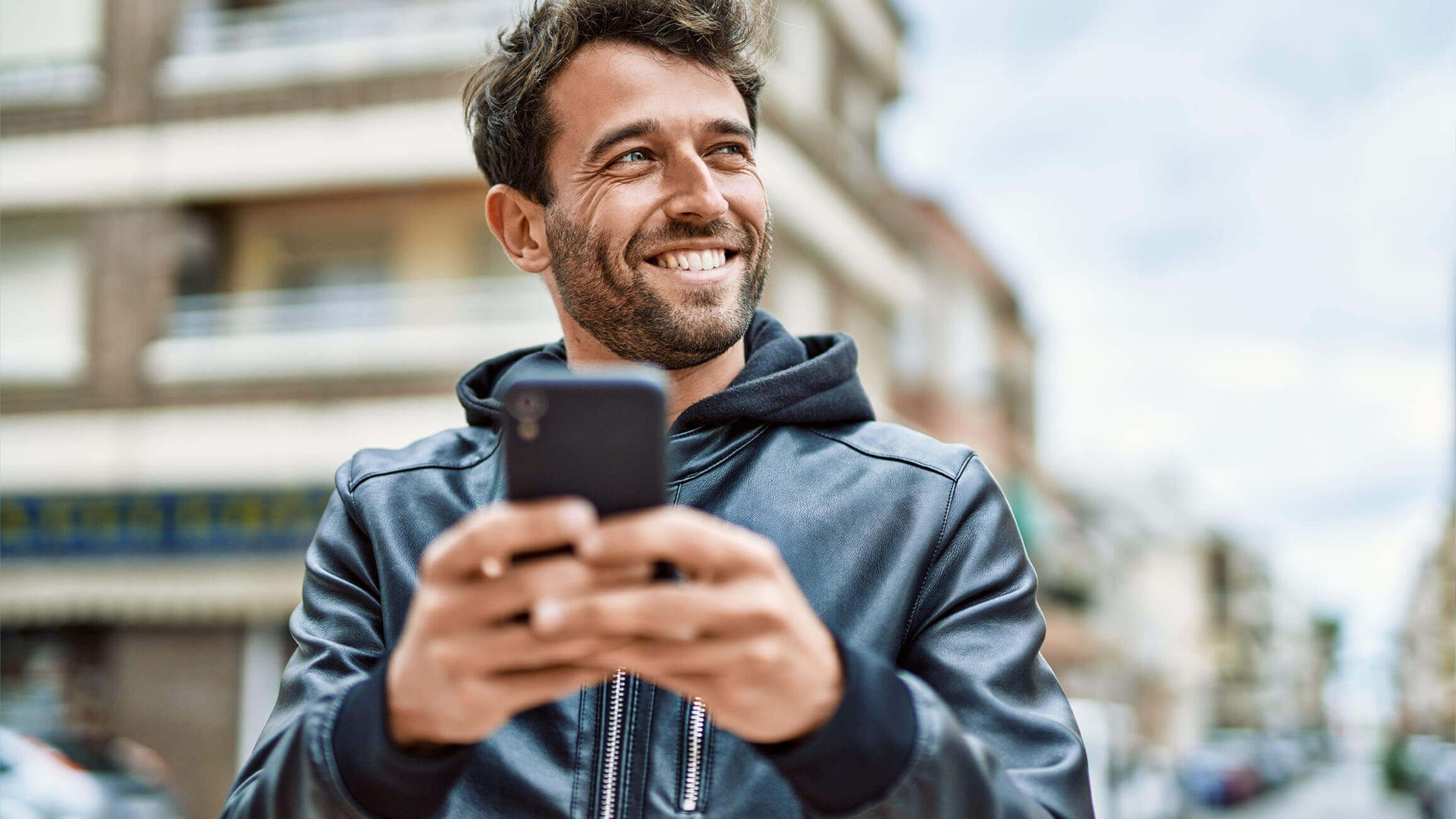Úspešný investor si pozerá vývoj svojich investícii v mobile na ulici a usmieva sa.