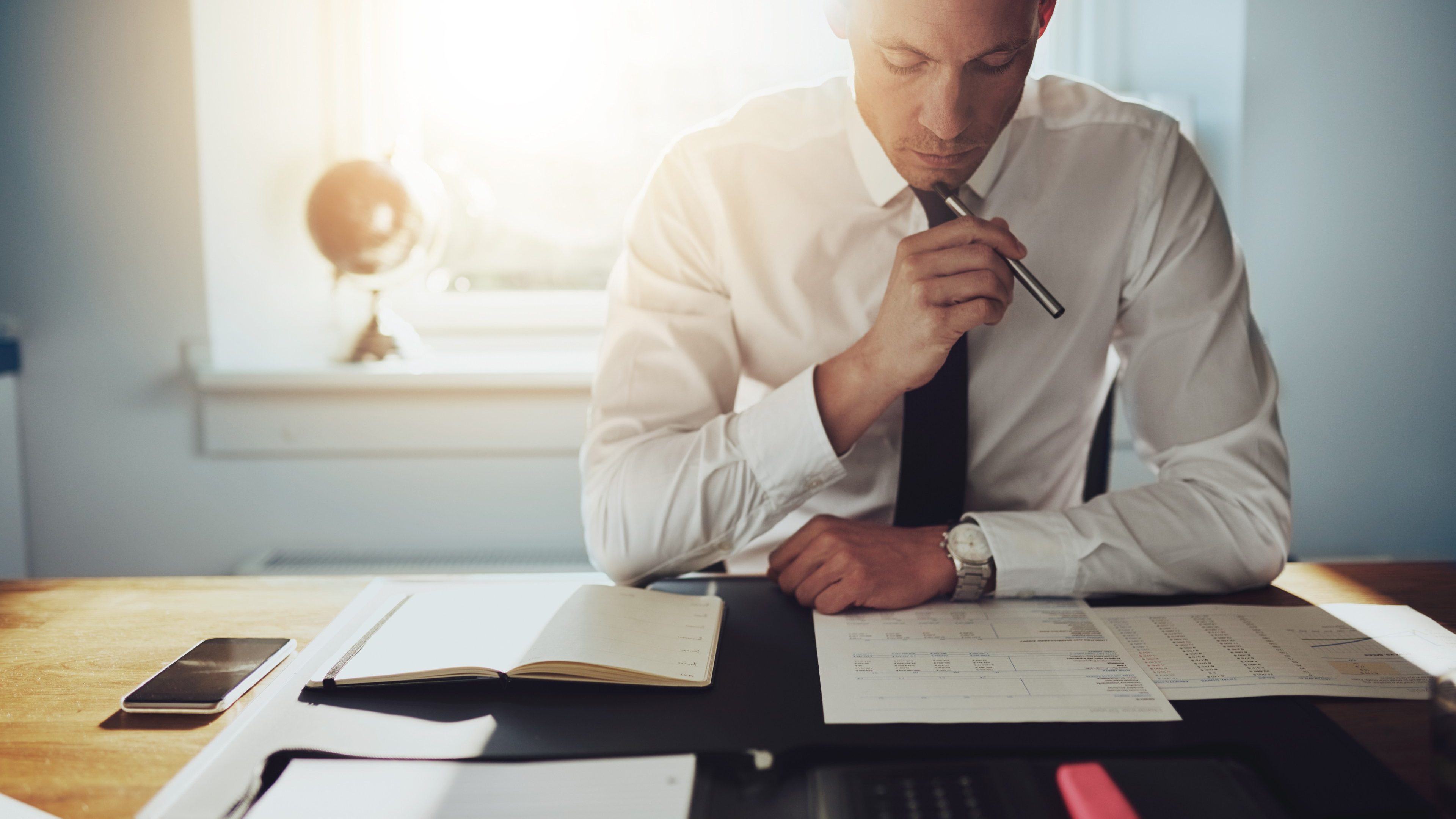 Serious business man working on documents looking concentrated with briefcase and phone on the table